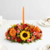 Orange candle in a low floral centerpiece with sunflowers and roses