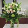 Large white and pale pink floral arrangement in a green glass vase