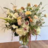 Tall arrangement of white hydrangeas, calla lilies, and pastel roses in a clear glass vase