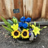 Arrangement of blue roses and yellow lilies with sunflowers in a rustic container