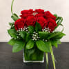 Red roses arranged in a clear square vase with white filler flowers