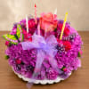 Round pink and purple floral arrangement with candles, a rose, and a ribbon on a white plate