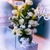 White calla lilies and roses arranged in a glass vase with a white ribbon