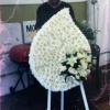Large white funeral wreath on a stand with a small bouquet of pale flowers