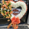 Heart-shaped floral tribute with white and orange flowers and a large orange bow