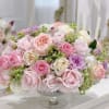 A pastel rose arrangement in a glass pedestal vase