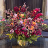 Colorful mixed bouquet in a gold vase with pink, orange, and burgundy blooms