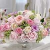 Pastel pink and lavender roses arranged in a clear pedestal vase