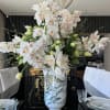 Large white orchid arrangement in a decorative vase on a dining table