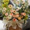 Mixed bouquet in a woven basket with peach, white, blue, and green flowers