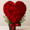 Heart-shaped arrangement of red roses in a black box with a red ribbon