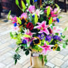 Large bouquet of pink lilies, roses, and sunflowers in a wrapped container