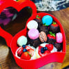 Heart-shaped red box filled with colorful macarons and chocolate-covered strawberries