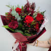 Hand-tied bouquet with red roses, red chrysanthemums, and berries wrapped in dark red paper.
