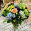 Mixed bouquet in a clear glass vase with peach roses and blue hydrangeas