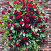 Large bouquet of red roses and carnations with greenery against a brick wall