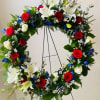 Circular floral wreath with red and white roses, white lilies, and blue accents