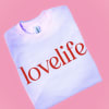 Folded white sweatshirt with red "lovelife" text on a pink background