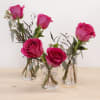 Pink roses in small clear glass vases on a wooden surface