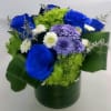 Blue roses and purple and white daisies in a green hatbox