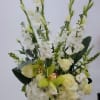 Tall white floral arrangement in a dark green vase with pale green orchids and roses