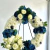 Circular floral wreath with white roses, blue hydrangeas, and white chrysanthemums on a stand