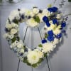 Heart-shaped floral wreath with white and blue flowers on a stand