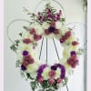Large floral wreath on a stand with pink roses, white mums, and purple flowers