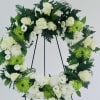 White floral wreath on a black stand with green accents