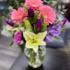 Mixed bouquet of pink gerbera daisies, purple tulips, and a pale lily in a glass vase