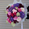 Hand-tied bouquet of pink, purple, and burgundy flowers wrapped in white paper
