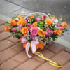 Basket arrangement of orange and pink roses with ribbon