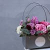 Pink and purple flowers arranged in a gray gift box with handles