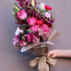 Hand-tied bouquet of pink and magenta flowers wrapped in brown paper