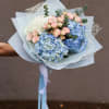 Hand-tied bouquet of blue hydrangeas, pink spray roses, and white blooms