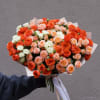 Large bouquet of orange, peach, and white roses wrapped in paper