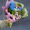 Handheld bouquet of blue, pink, and white flowers wrapped in pastel paper