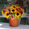 Sunflowers, pink roses, and white daisies in a tall orange vase