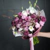 Handheld bouquet of pink, purple, and white flowers wrapped in paper