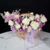 Basket arrangement of white roses and purple daisies with a lavender ribbon
