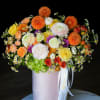 Mixed bouquet of orange, yellow, white, and purple flowers in a pink hat box