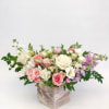 Low floral arrangement of pink, white, and lavender roses in a square vase