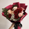 Handheld bouquet of red and blush roses wrapped in burgundy paper