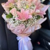 Large bouquet of pink lilies, roses, and white filler flowers wrapped in pink paper with ribbon