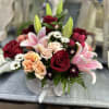 Mixed bouquet of red roses, pink lilies, and peach spray roses in a white hatbox