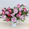 Pink and lavender roses arranged in a white pedestal vase