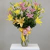 Tall clear vase of pink and yellow lilies with buds, tied with a pink and yellow ribbon bow.
