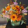 Mixed bouquet of orange gerbera daisies, peach roses, and pink blooms in a glass vase