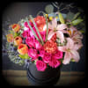 Bright mixed bouquet of pink roses, lilies, and orange tulips in a black hatbox