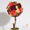 Round floral arrangement on a branch-like stem with pink, purple, and cream blooms